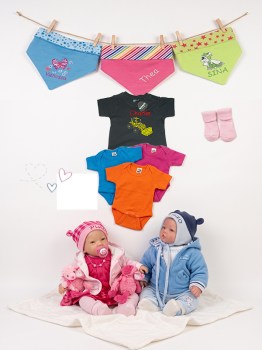 Personalisierte Babykleidung: Babypuppen in Rosa und Blau, bunte Bodys, besticktes T-Shirt und Halstücher vor weißem Hintergrund.