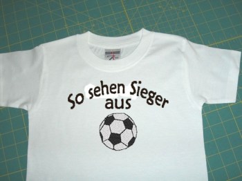 Baby Shirt in weiss mit dem Schriftzug, So sehen Sieger aus, und mit einem Fussball bestickt.