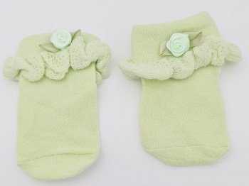 Erstlingssocken in hellgrün mit Rüsche und kleinem Blümchen liegend