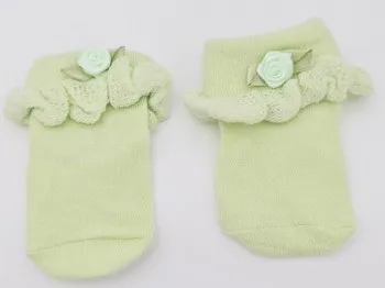 Erstlingssocken in hellgrün mit Rüsche und kleinem Blümchen liegend